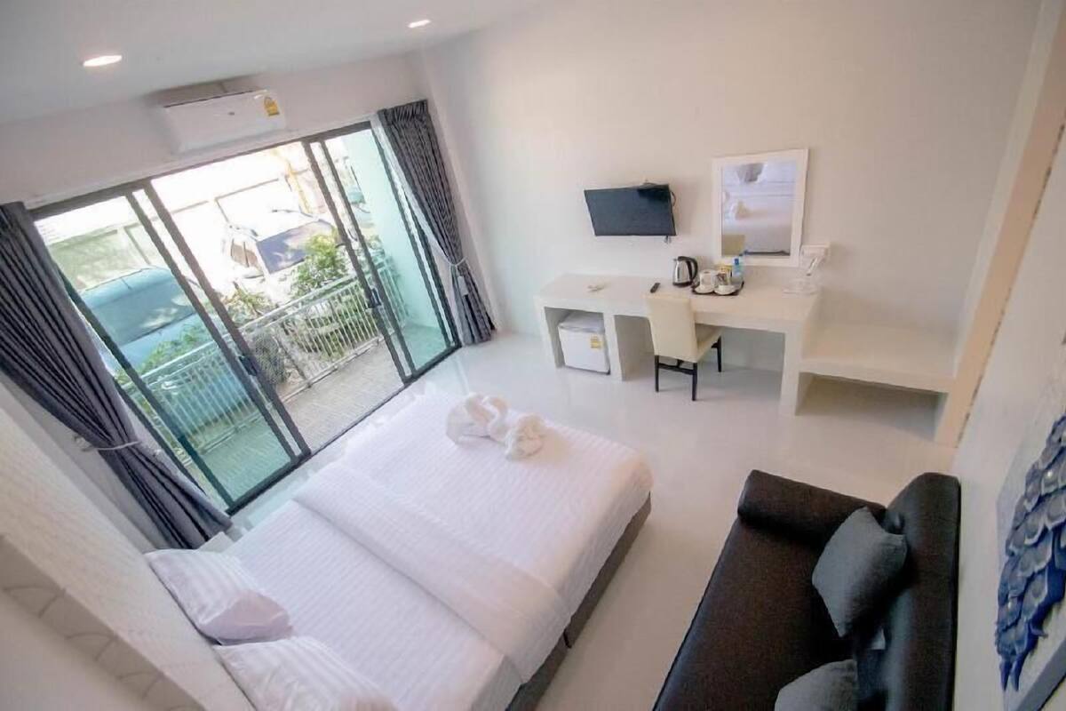 A hotel room with a bed, a desk, a TV, and a balcony with a view of the outside.