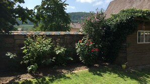 A rustic wooden building with a stone wall and a garden with various plants and flowers.