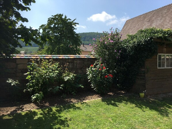 Een rustiek houten gebouw met een stenen muur en een tuin vol planten en bloemen.