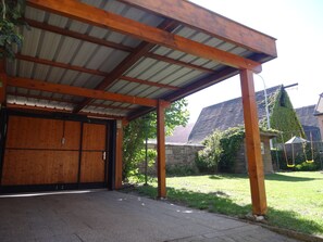 Een overdekt buitengebied met een houten constructie, een metalen dak en een stenen muur.