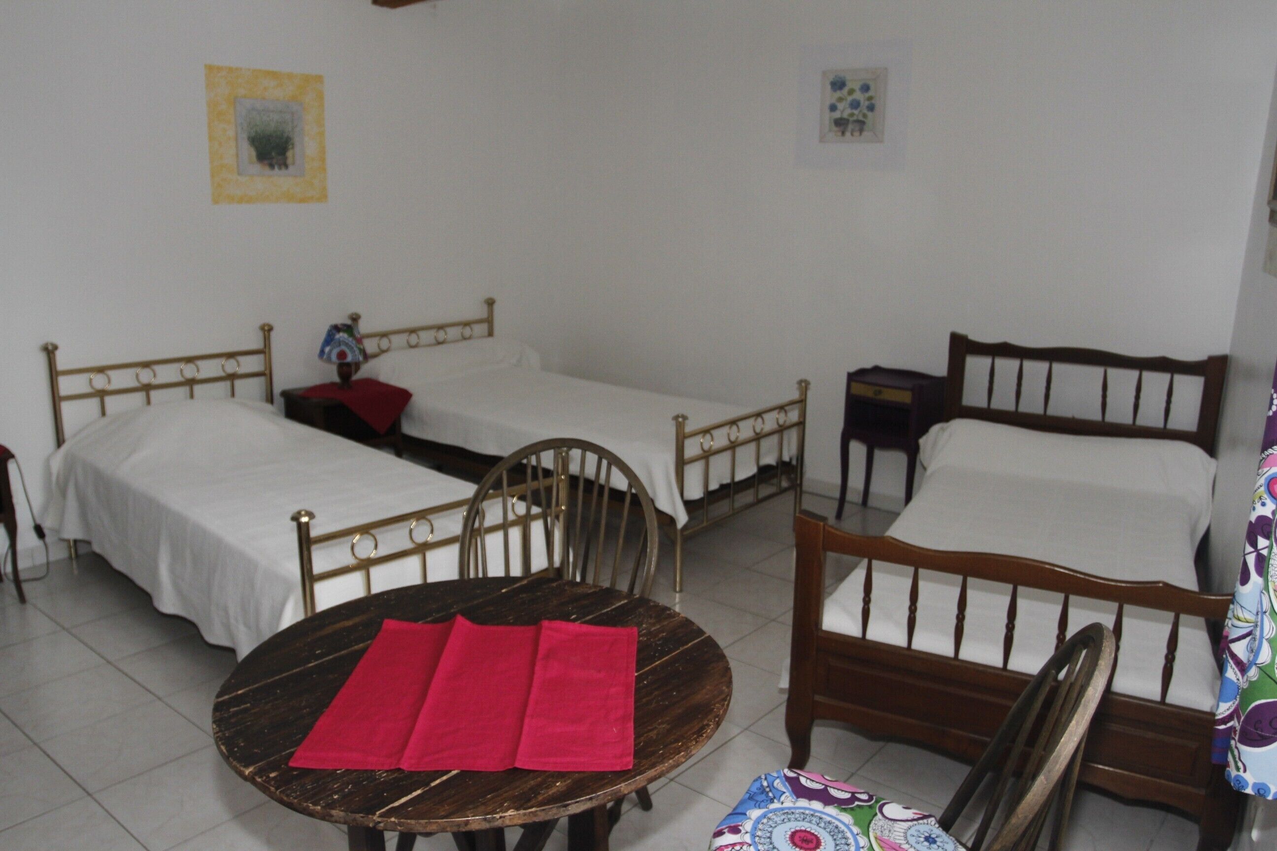 A room with two single beds, a round wooden table with red napkins, and a chair.