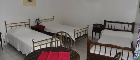 A room with two single beds, a round wooden table with red napkins, and a chair.