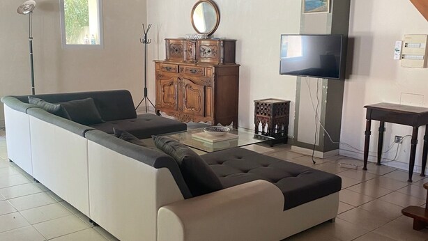 A modern living room with a sectional sofa, wooden ceiling beams, a television, and a small table. - Gîtes in Camargue (Arles)