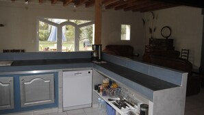 A kitchen with a built-in dishwasher, a sink, and a countertop with various kitchen items. There is a window with a view of the outdoors. - Gîtes in Camargue (Arles)