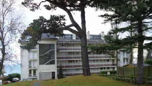 A multi-story residential building with a central staircase, surrounded by a grassy area and trees. - Nice apartment with sea view a few meters away and balcony, close to shops. (Perros-Guirec)