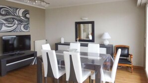 A modern dining area with a glass table, white chairs, a black TV stand, and a mirror on the wall. - Nice apartment with sea view a few meters away and balcony, close to shops. (Perros-Guirec)