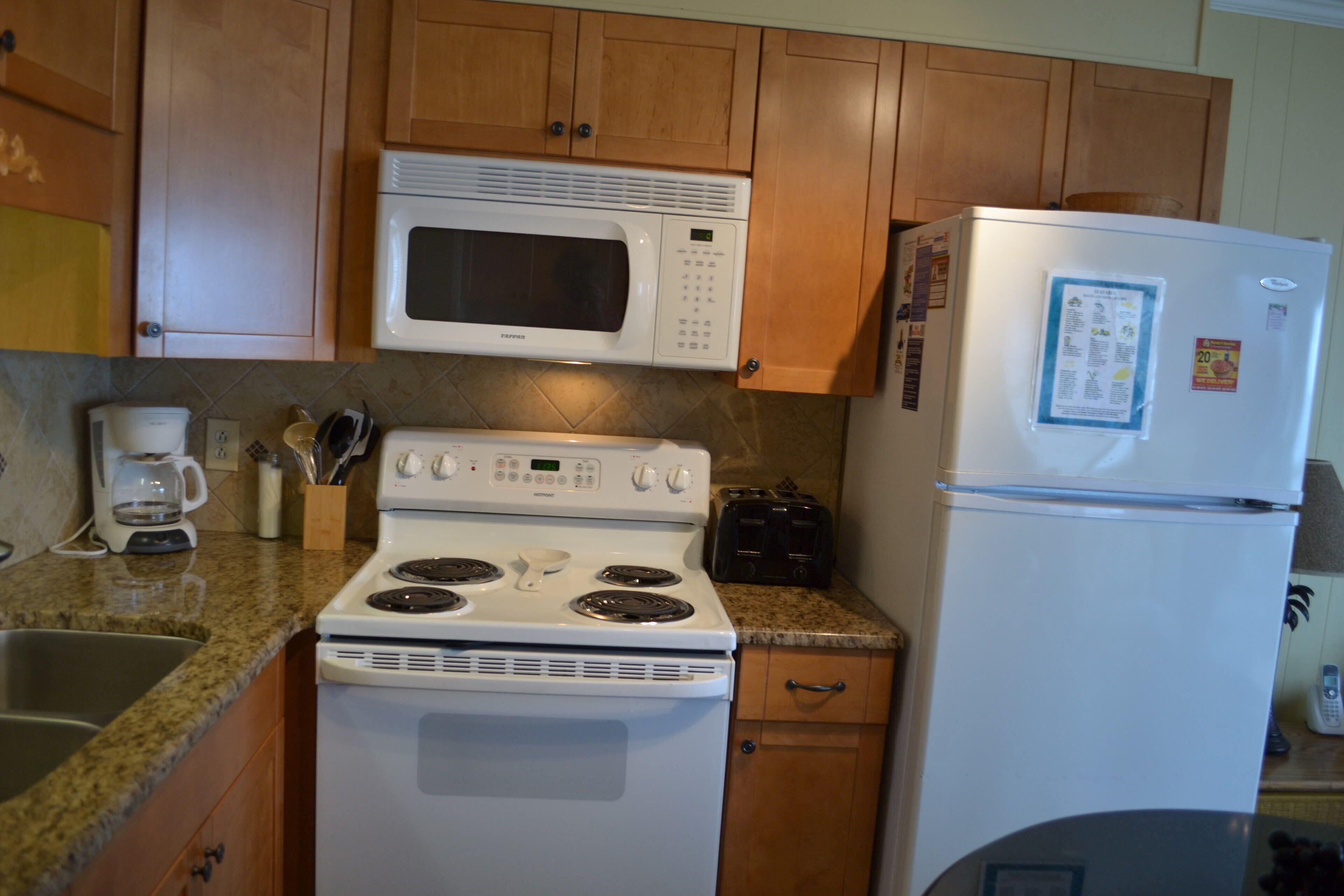 A kitchen with wooden cabinets, a white stove, a microwave, and a refrigerator.