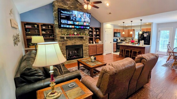 A living room with a fireplace, a television, and a kitchen in the background.