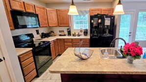 A kitchen with wooden cabinets, a black refrigerator, a microwave, a stove, a sink, and pendant lighting.