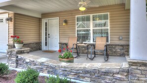 A covered porch with a ceiling fan, a stone wall, a door, and a window with blinds.