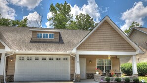 A two-story house with a garage, a small porch with a table and chairs, and a stone foundation.