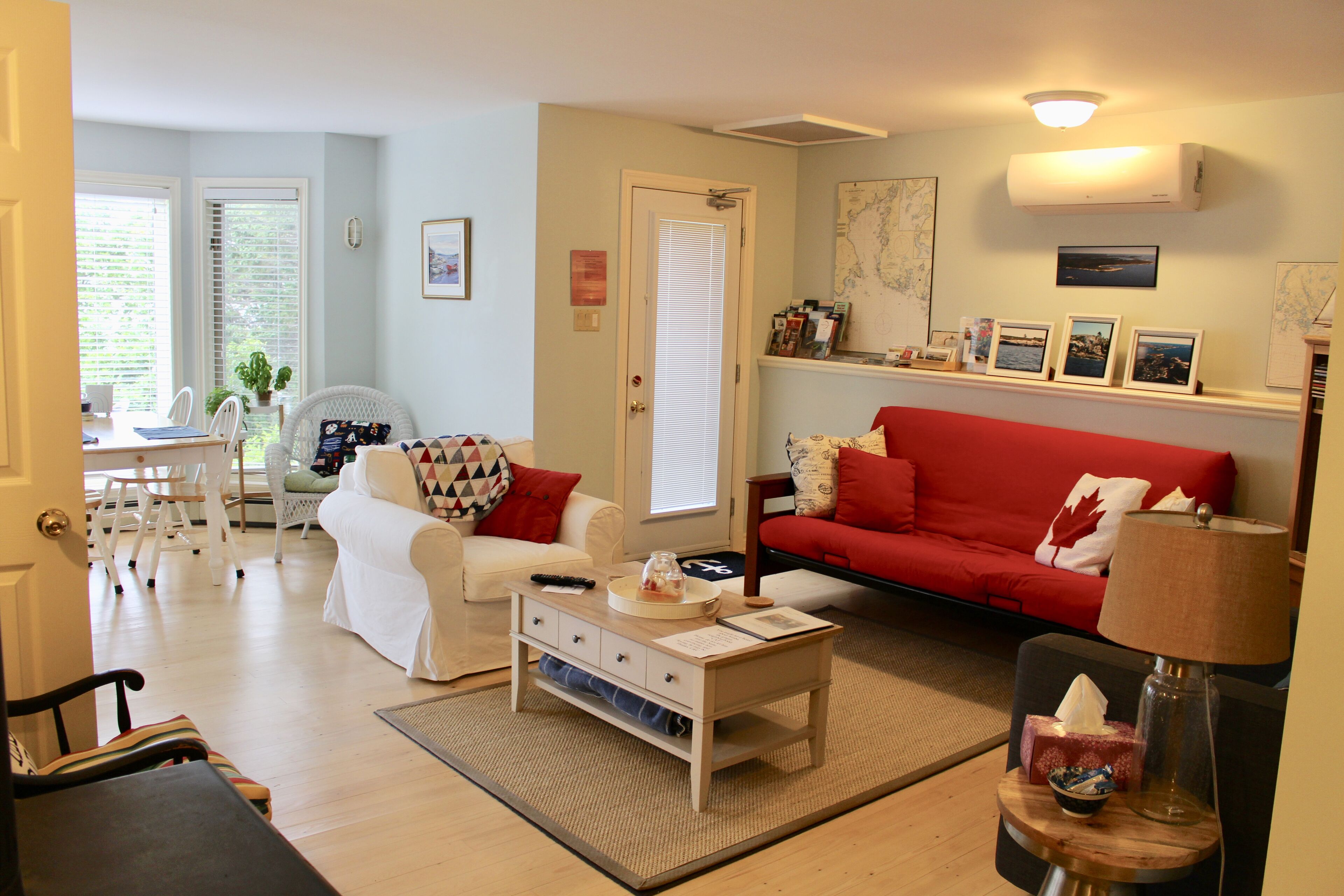 A living room with a red sofa, white armchairs, a coffee table, and a dining area with a white table and chairs.