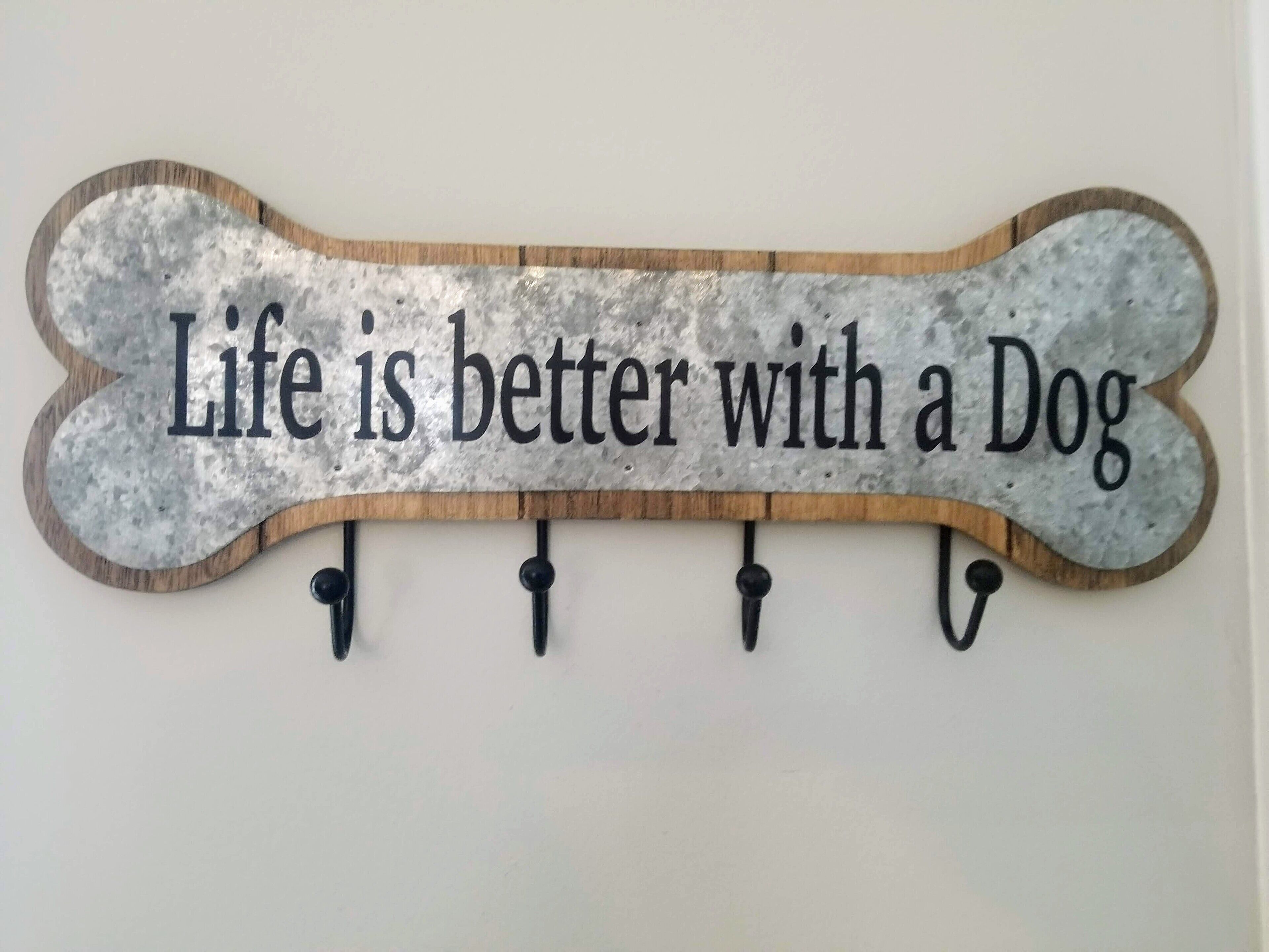 A wall-mounted sign with the text "Life is better with a Dog" on a bone-shaped background.