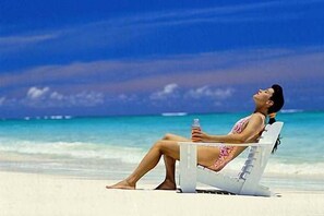 En person ligger afslappet i en strandstol med en flaske og ser ud over havet.