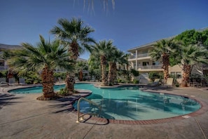 A swimming pool area with palm trees and a building in the background.