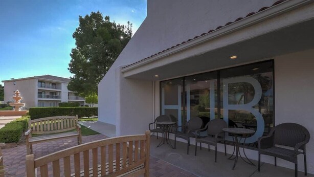 Exterior de un hotel con un patio que incluye un banco, mesas y una fuente.