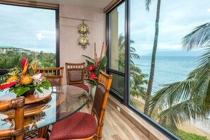 A dining area with a glass table, wicker chairs, and a view of the ocean.
