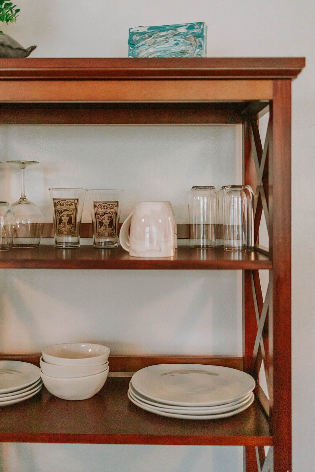 A wooden shelf with various glassware and plates.
