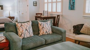 A living room with a green sofa, two patterned pillows, a wooden coffee table, and a white armchair. There is a dining table with chairs in the background. - Only 1 block to FRONT BEACH! Perfect location in Ocean Springs! The King Suite (Ocean Springs)