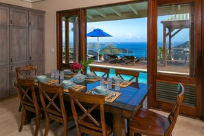 A dining area with a view of the ocean, wooden furniture, and a blue umbrella. - Villa Ixora Sleeps 2-10 people~ 5 bedrooms, 4 baths, pool, AMAZING views! (St.john)