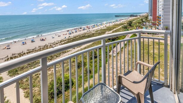 A balcony with a view of a beach, a pier, and a hotel building. - Scenic Views  Atlantica Resort 🏖️ Ocean Front🏖️ (Myrtle Beach)