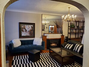A living room with a blue sofa, a black sofa, a glass coffee table, a fireplace, a chandelier, and a large mirror. - 3 floors character house (Winnipeg)