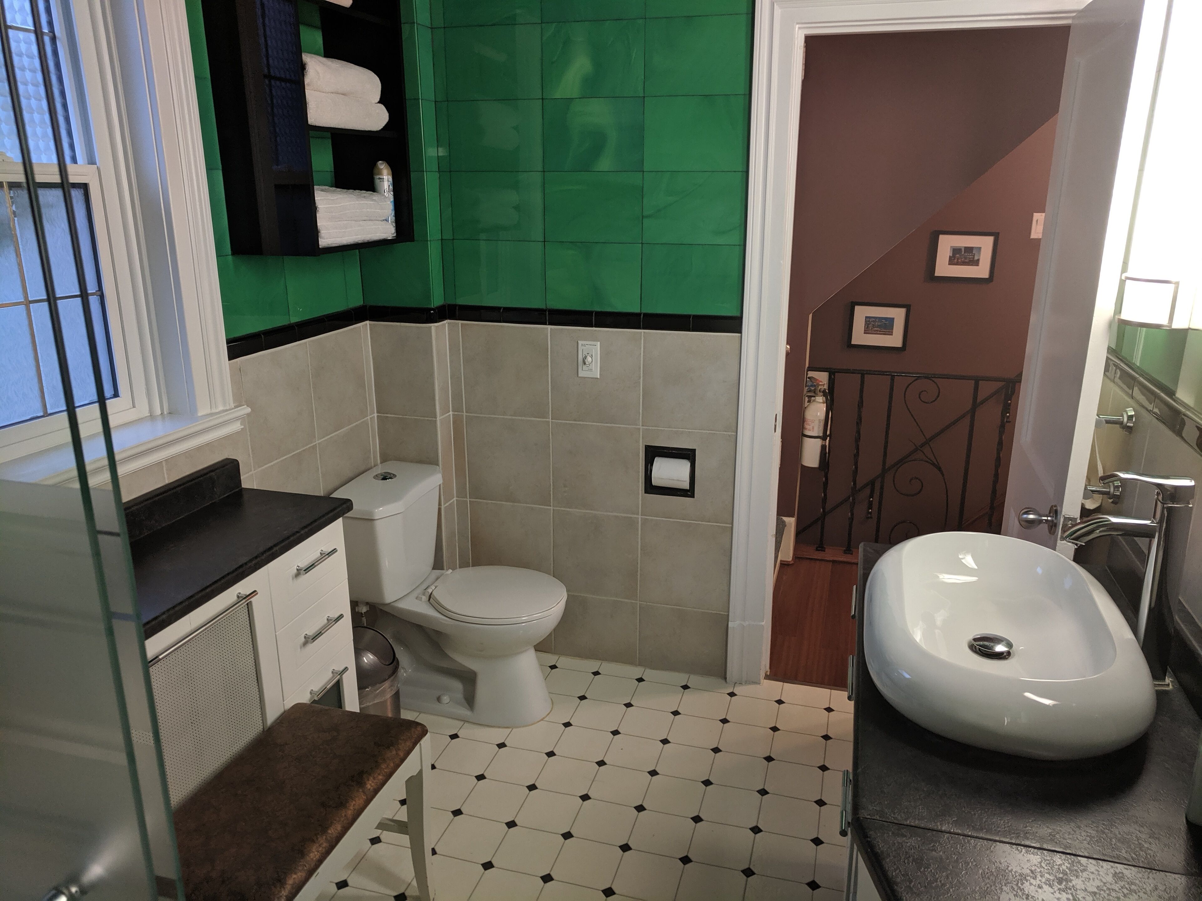 Ein Badezimmer mit Toilette, Waschbecken und Spiegel. Eine grüne Wand und ein Fenster mit Jalousien.