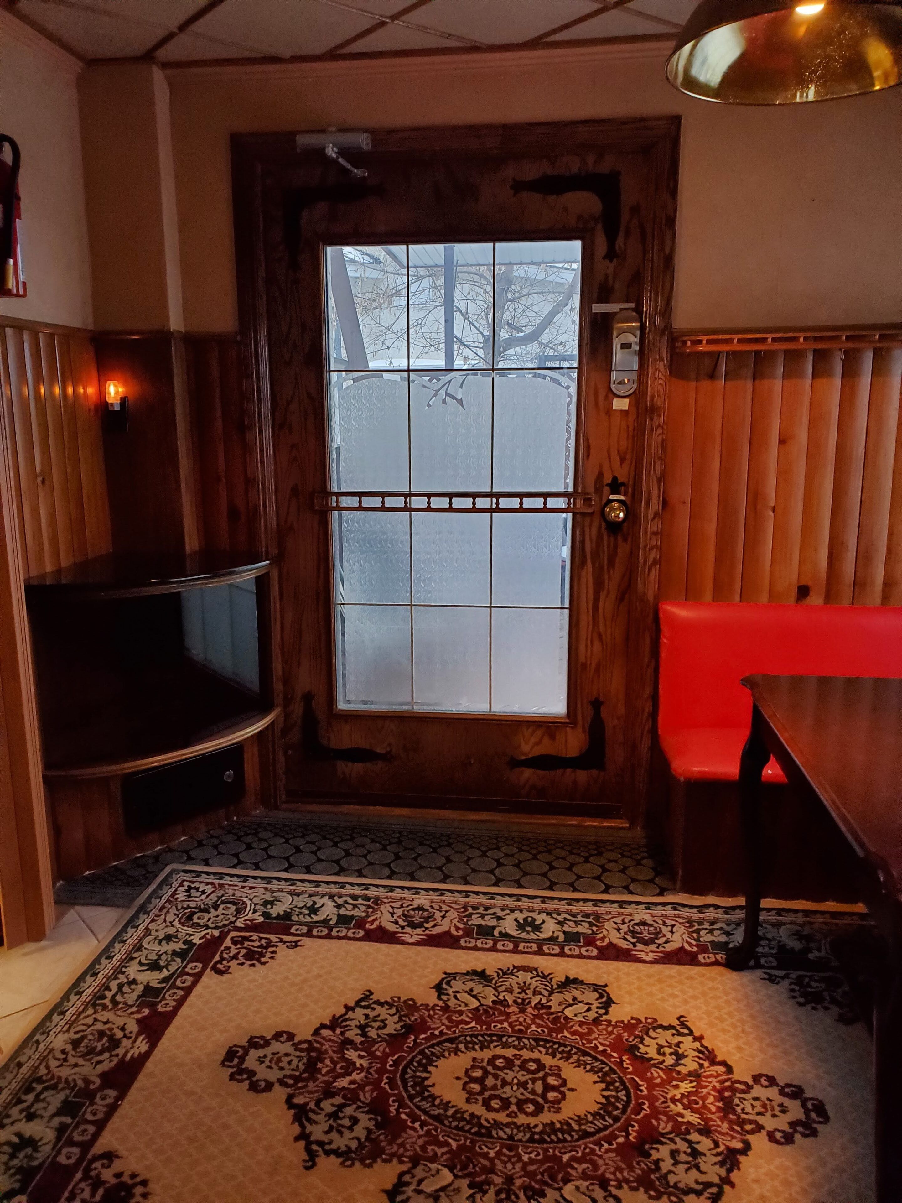 A wooden door with a frosted glass panel, a patterned rug, a red bench, and a television on the left.
