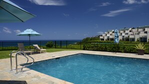 A swimming pool with a view of the ocean, a fence, and a building in the background.