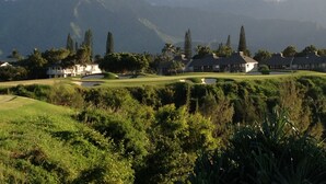 A golf course with a clubhouse, lush greenery, and mountains in the background.