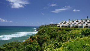A coastal hotel with ocean views, lush greenery, and a clear sky.