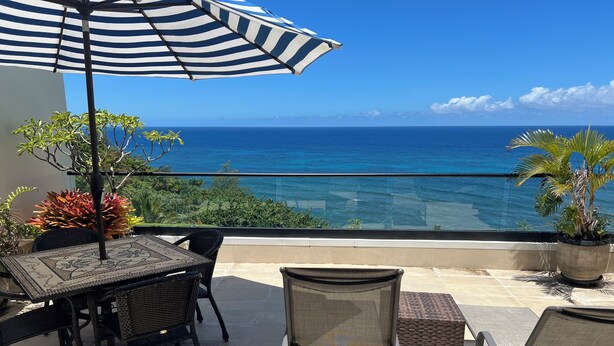 A terrace with a table and chairs, a striped umbrella, and a view of the ocean.