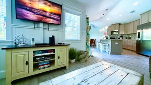 A modern kitchen with a large island, wooden flooring, and a flat-screen TV mounted above the island. - Beach Time AMI! Pet Friendly Home with Pool, Hot Tub and Walk to Beach (Holmes Beach)