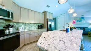 A modern kitchen with granite countertops, stainless steel appliances, and pendant lighting. - Beach Time AMI! Pet Friendly Home with Pool, Hot Tub and Walk to Beach (Holmes Beach)