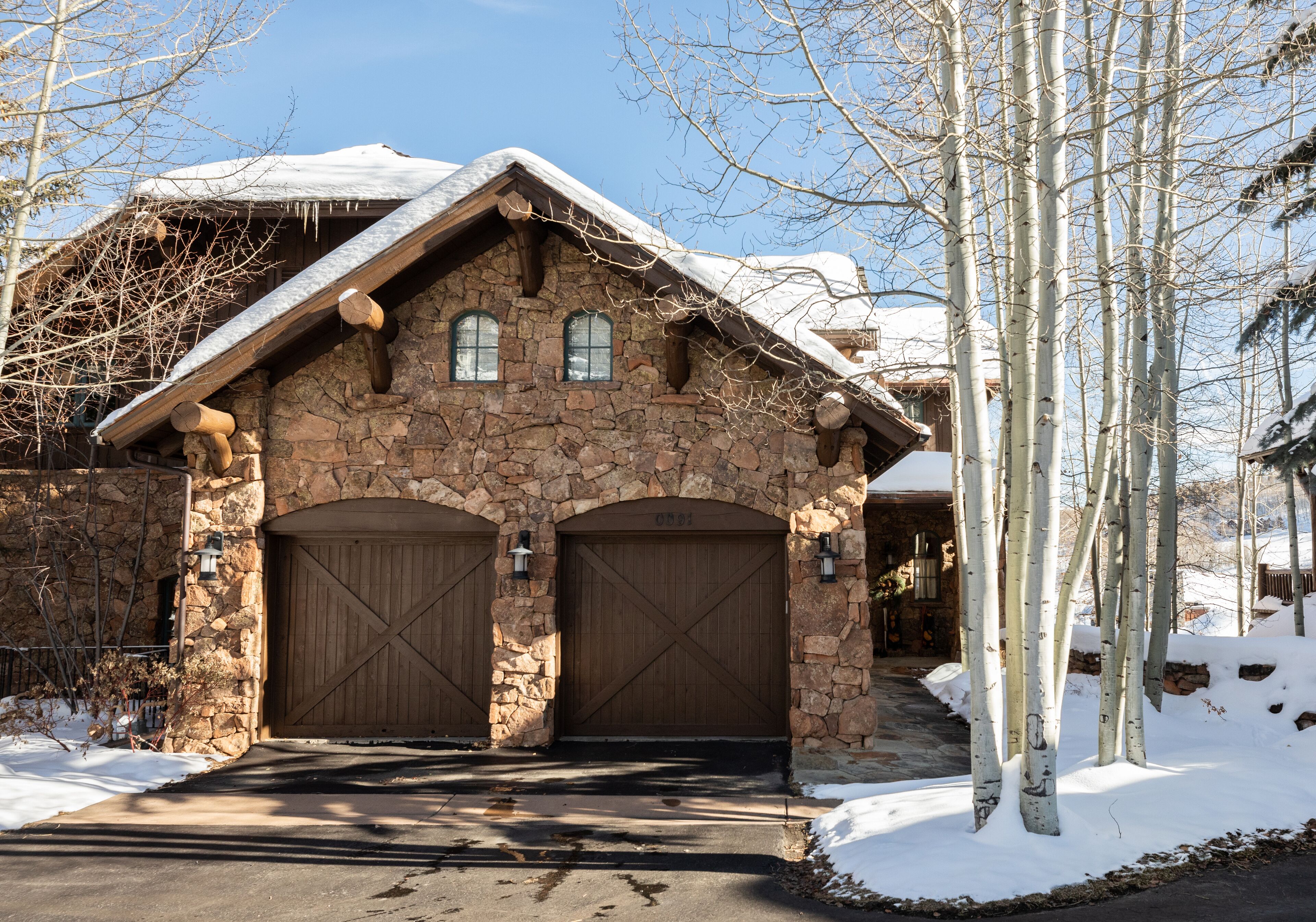 A stone building with two large wooden garage doors, a sloped roof, and a snow-covered landscape.
