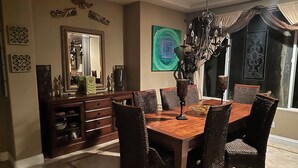 A dining area with a wooden table, wicker chairs, a chandelier, and decorative wall art. - Legoland Beach 1.5mi canyon golf  Four Seasons Aviara Carlsbad-1/2 acre- (Carlsbad)