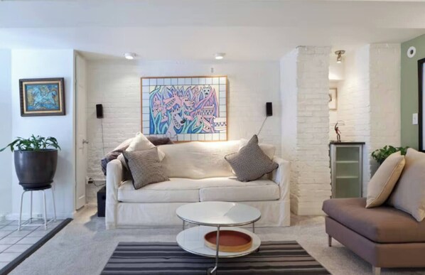 A modern living room with a white sofa, a coffee table, and a colorful abstract painting on the wall.
