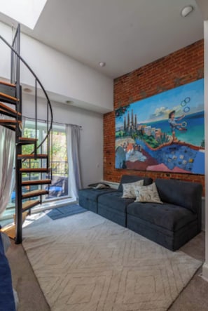 Un salon moderne avec un canapé bleu, un escalier en colimaçon et une fresque murale.