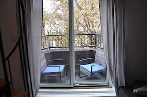 Une pièce dotée d’une porte-fenêtre coulissante donnant sur un balcon extérieur, où se trouvent deux chaises bleues et une table.