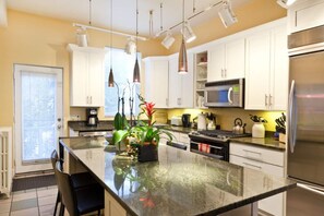A modern kitchen with white cabinets, stainless steel appliances, and a central island with plants.
