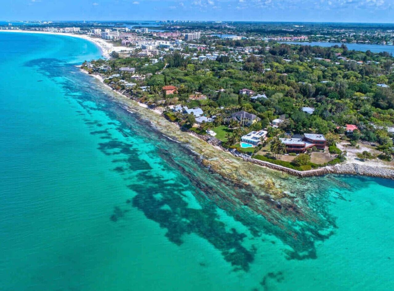 Luftaufnahme einer Küstenlandschaft mit Strand, Wohnhäusern und blauem Meer.
