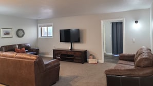 Un salon spacieux avec deux canapés en cuir marron, un téléviseur à écran plat, un meuble de rangement en bois et un petit objet décoratif posé sur le sol.