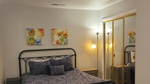Une chambre à coucher comprenant un lit, deux tables de chevet, une lampe sur pied et deux tableaux représentant des fleurs, accrochés au mur.