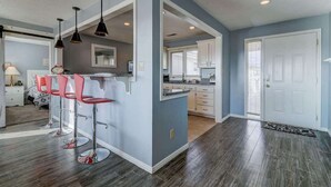 A modern kitchen with bar stools, a dining area with a table and chairs, and a separate dining room with a window.