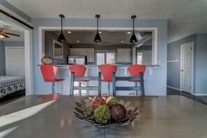 A modern kitchen with a dining area, featuring a central island with a fruit bowl, red chairs, and pendant lighting. - Las Palmas Resort #411 | All-Inclusive Amenities (Saint George)