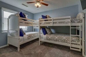 A room with bunk beds, a ceiling fan, and a window with blinds.