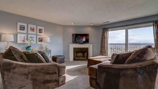 A living room with a fireplace, a television mounted above it, and a view of the outdoors through a large window.