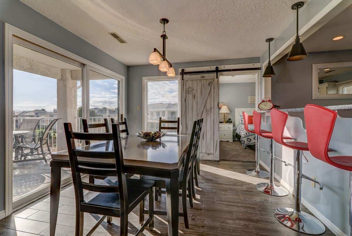 A dining area with a large table and chairs, a bar area with red bar stools, and a view through large windows.