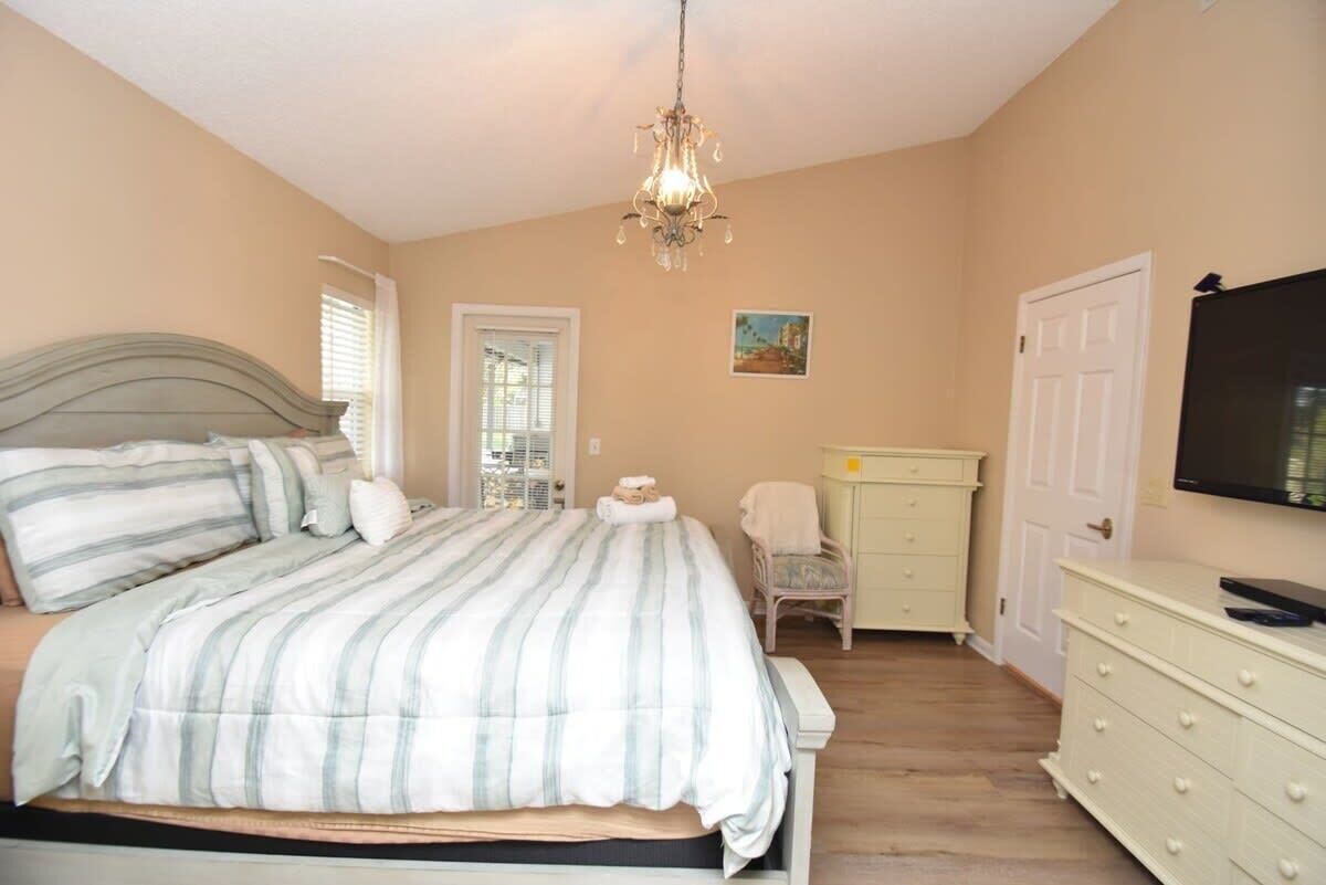 A bedroom with a bed, a dresser, a chair, a television, and a chandelier.