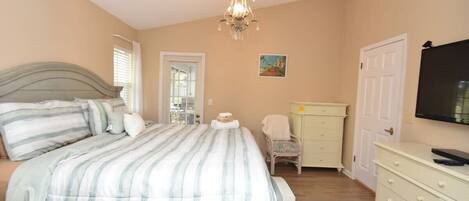 A bedroom with a bed, a dresser, a chair, a television, and a chandelier.